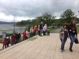 Die Gruppe geht eine Treppe hoch. Der See ist im Hintergrund zu sehen. Im Vordergrund wird ein blindes Mitglied von einer Begleitperson geführt.